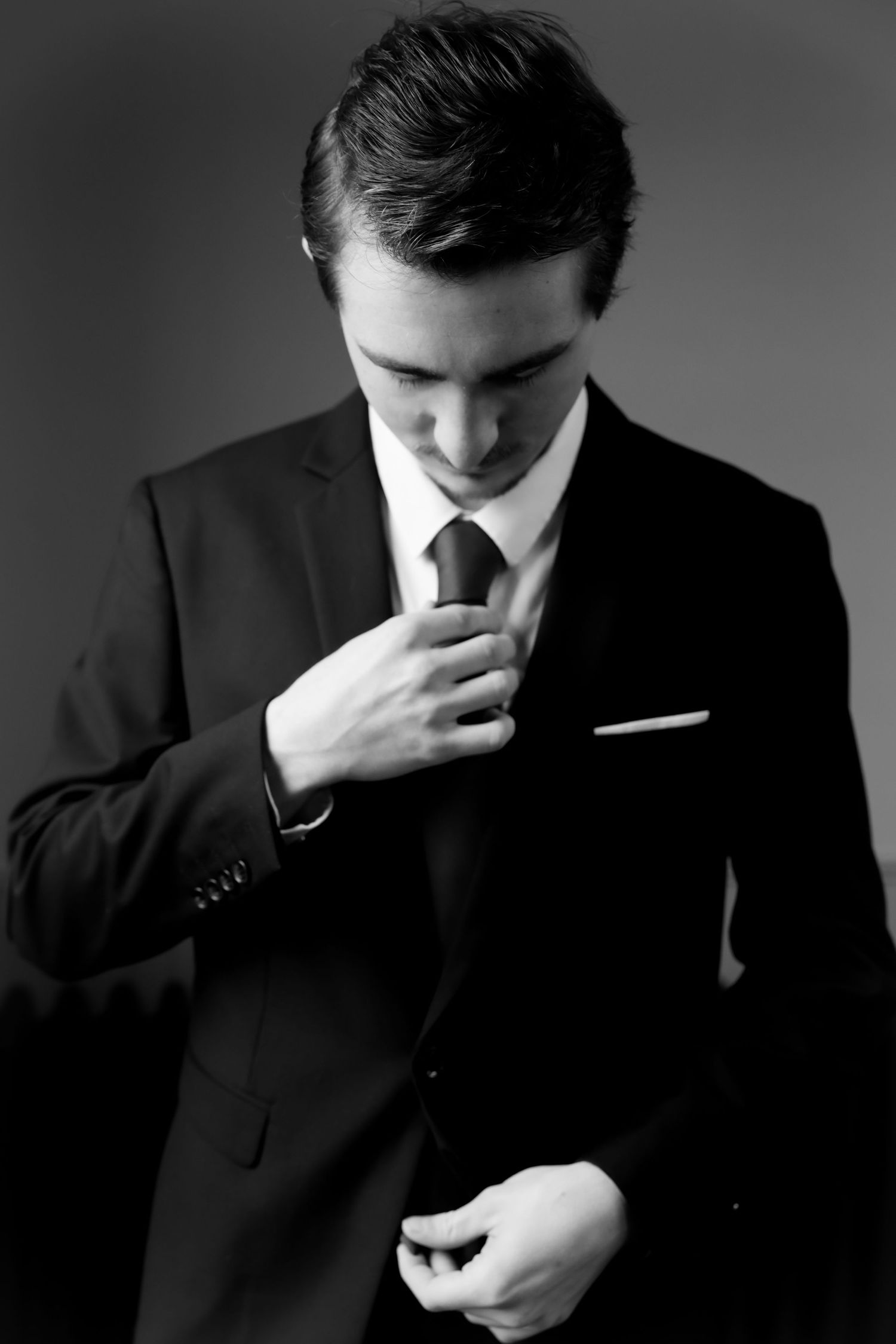 Elegant groom in black suit adjusting his tie in a sophisticated black and white wedding portrait.