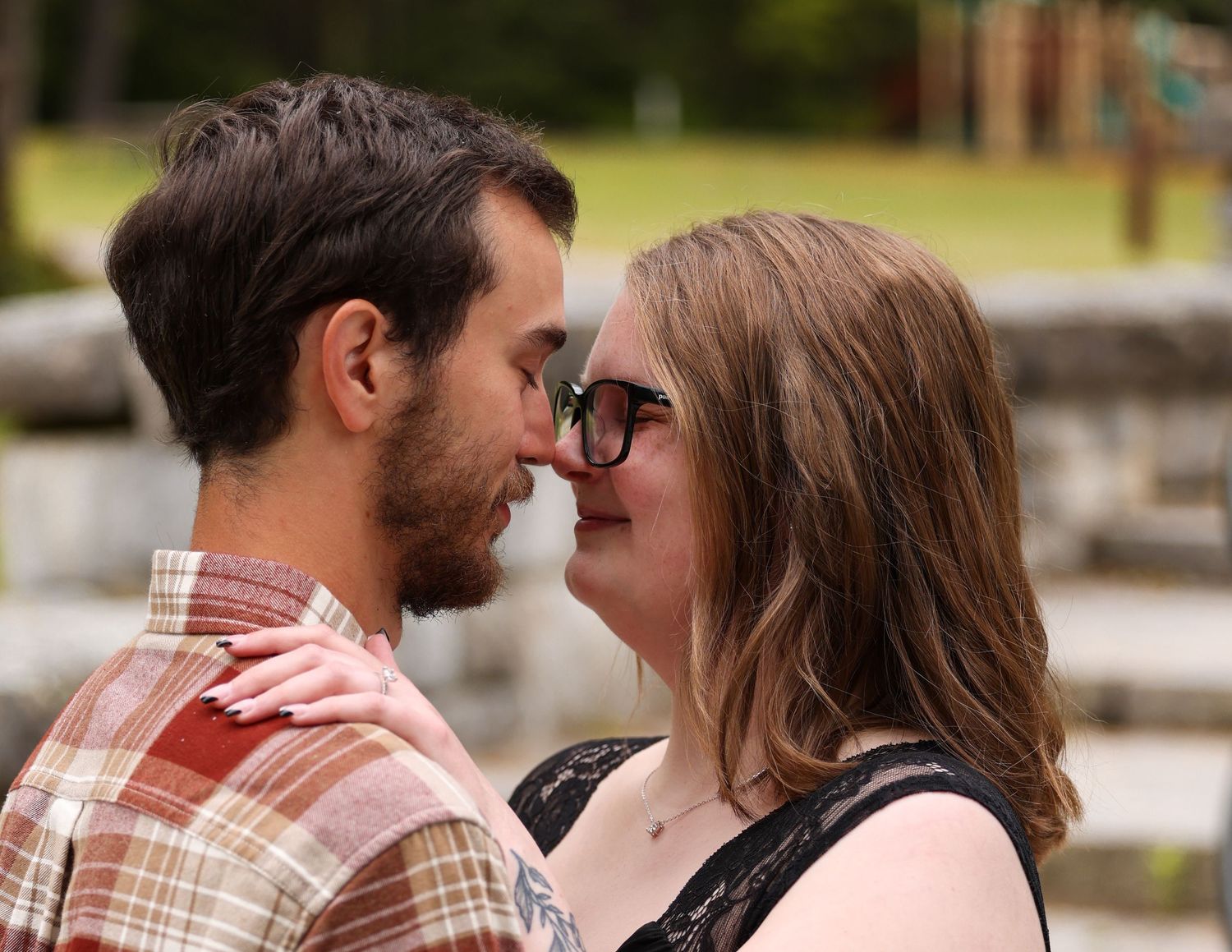 Couple shares a romantic nose-to-nose moment outdoors in a park setting.