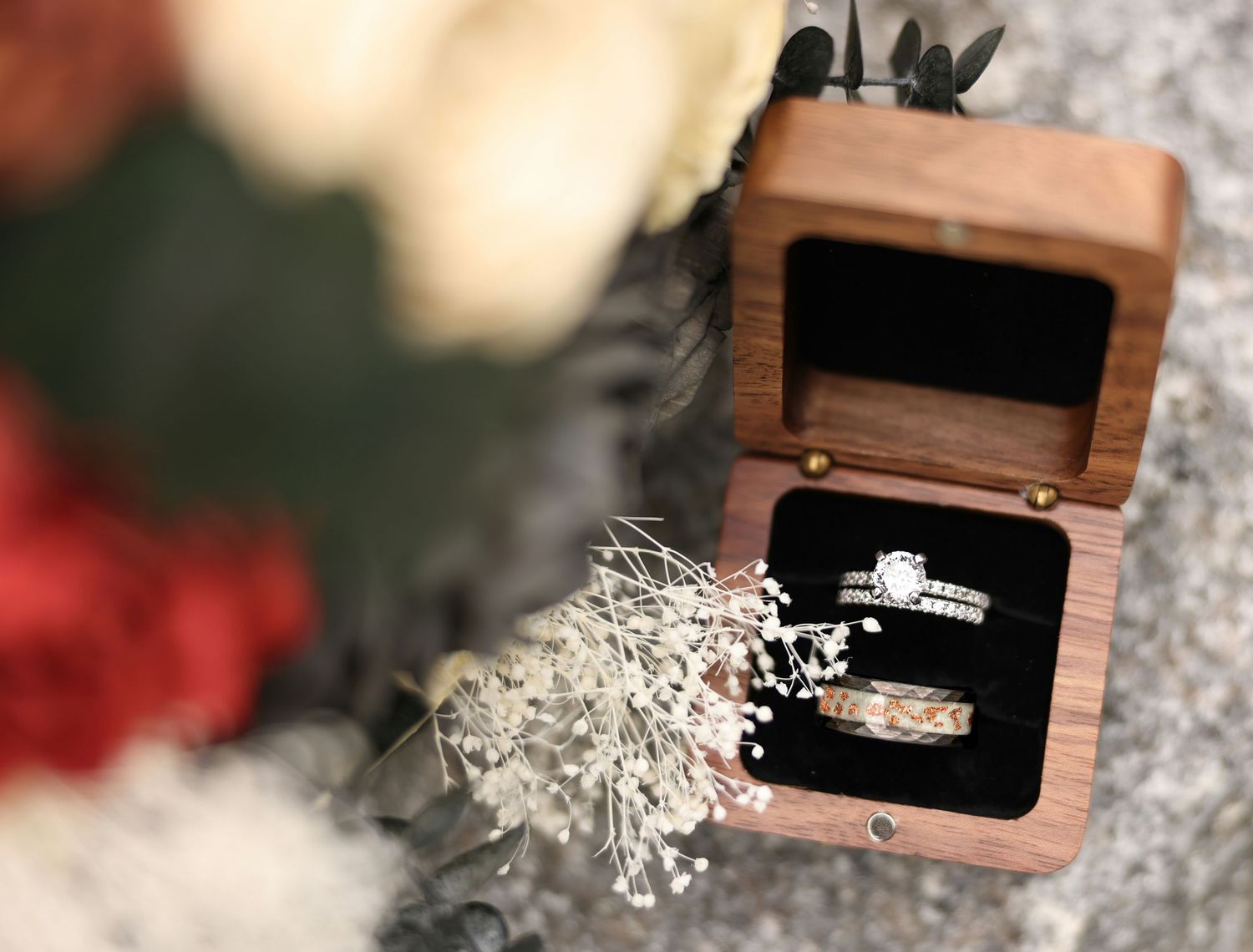 Wedding rings displayed in a wooden ring box with dried flowers in the foreground.