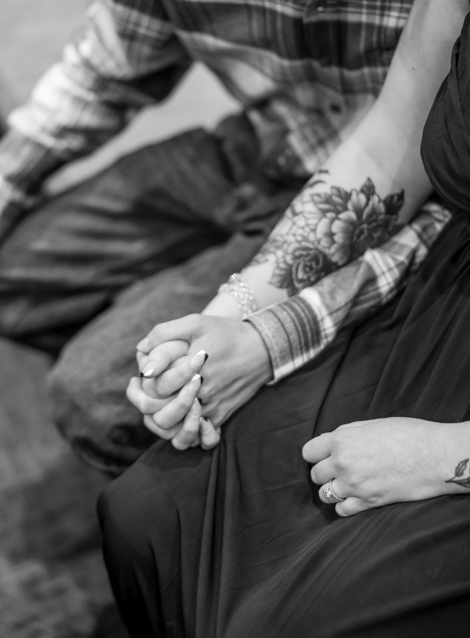 Black and white close-up of couple holding hands, womans arm featuring floral tattoo sleeve.
