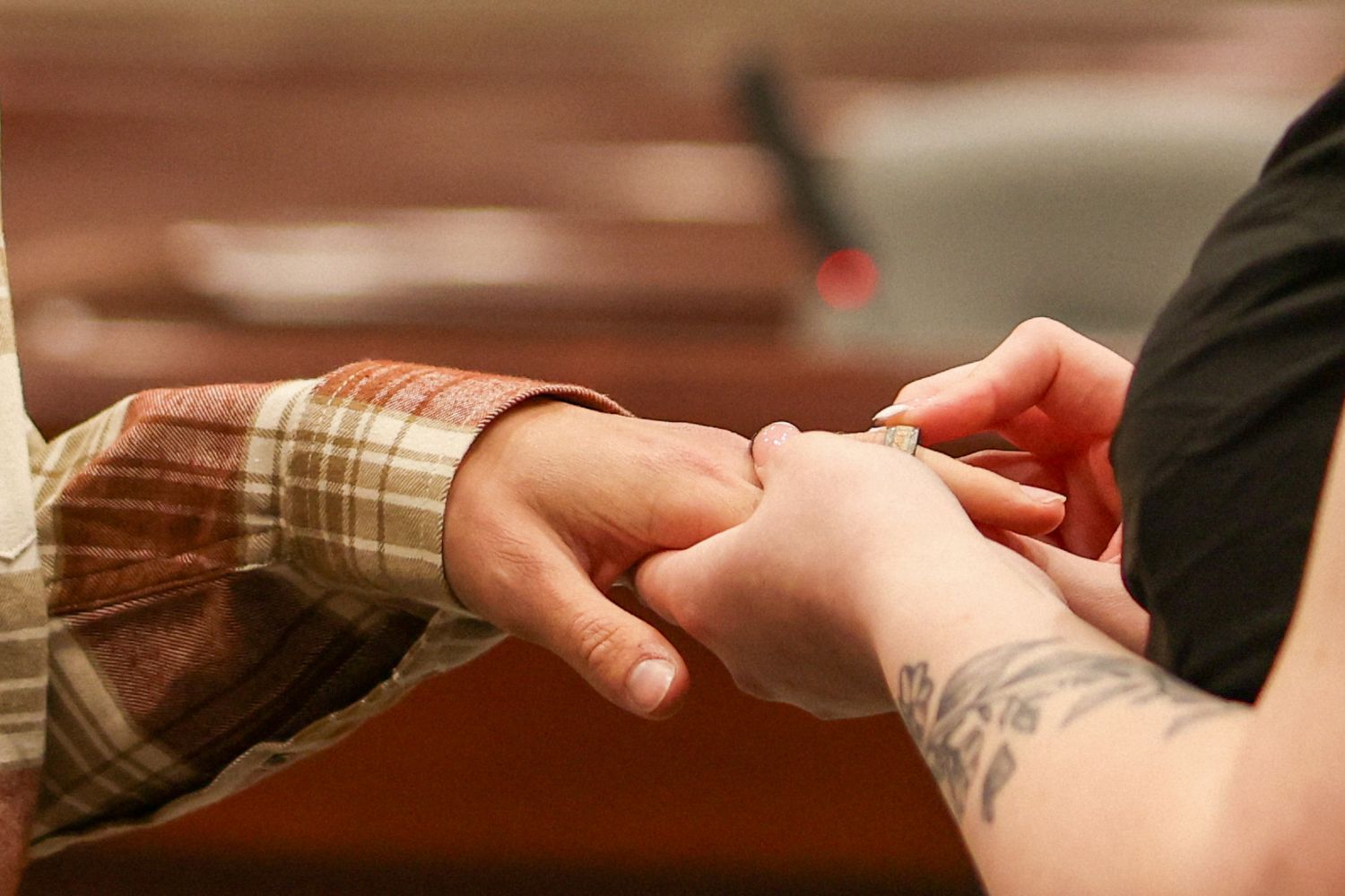 Close-up of tattooed hands exchanging a wedding ring during an indoor ceremony.