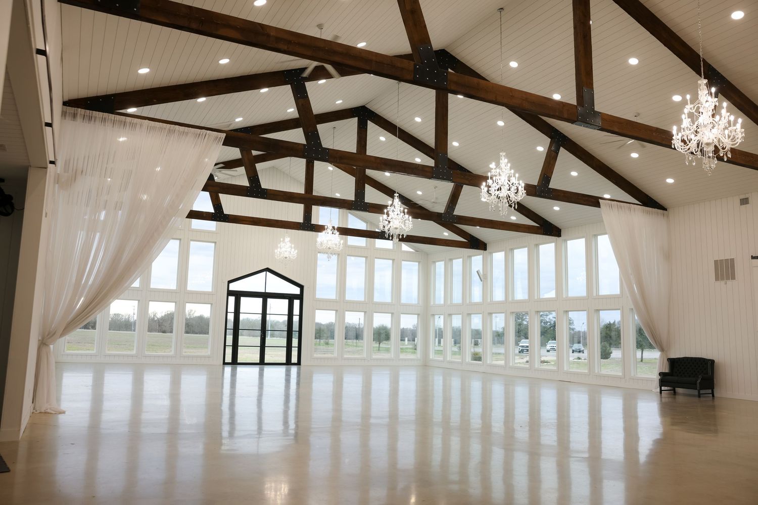 Elegant wedding venue with vaulted ceilings, wooden beams, chandeliers, and large windows.
