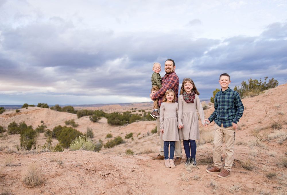 Family portrait taken in a desert setting with dramatic cloudy skies overhead.