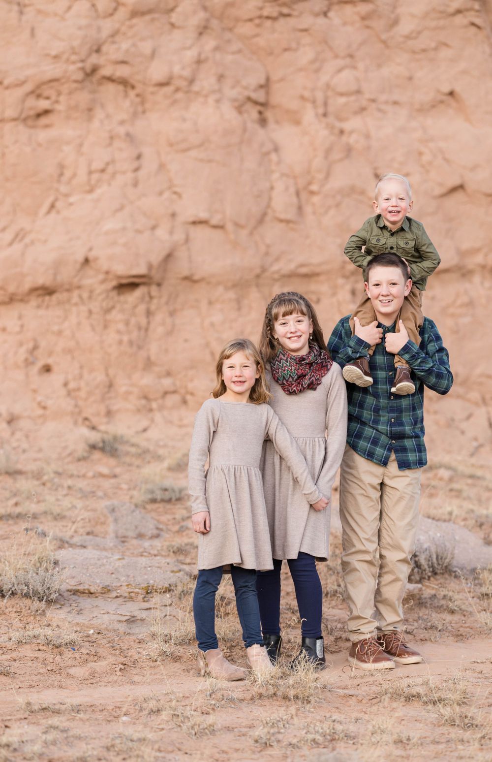 Sibling portrait with little brother on big brothers shoulders and sisters laughing.