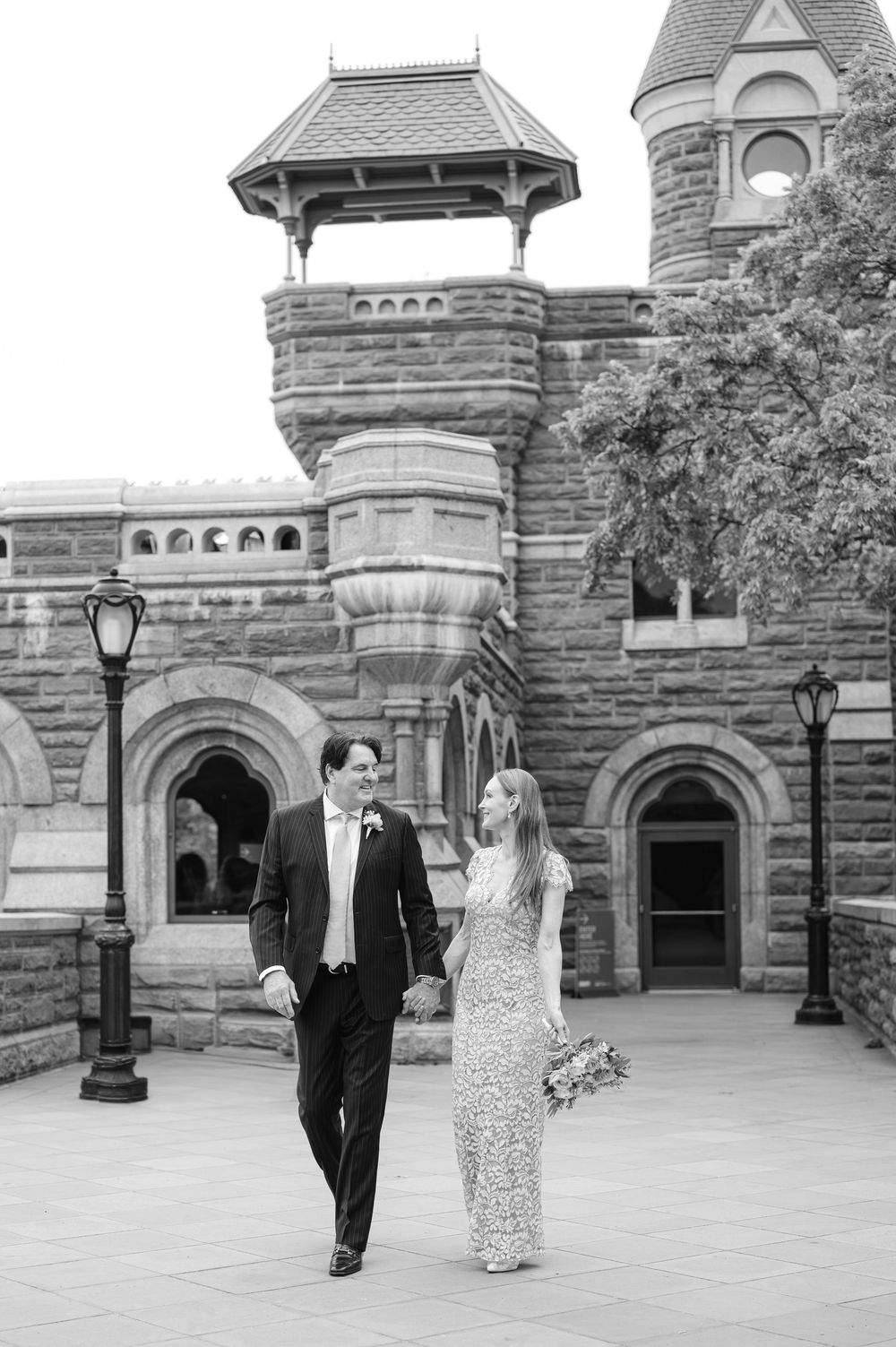 Black and white photo of bride and groom walking at Belvedere Castle in Central Park on their wedding day.