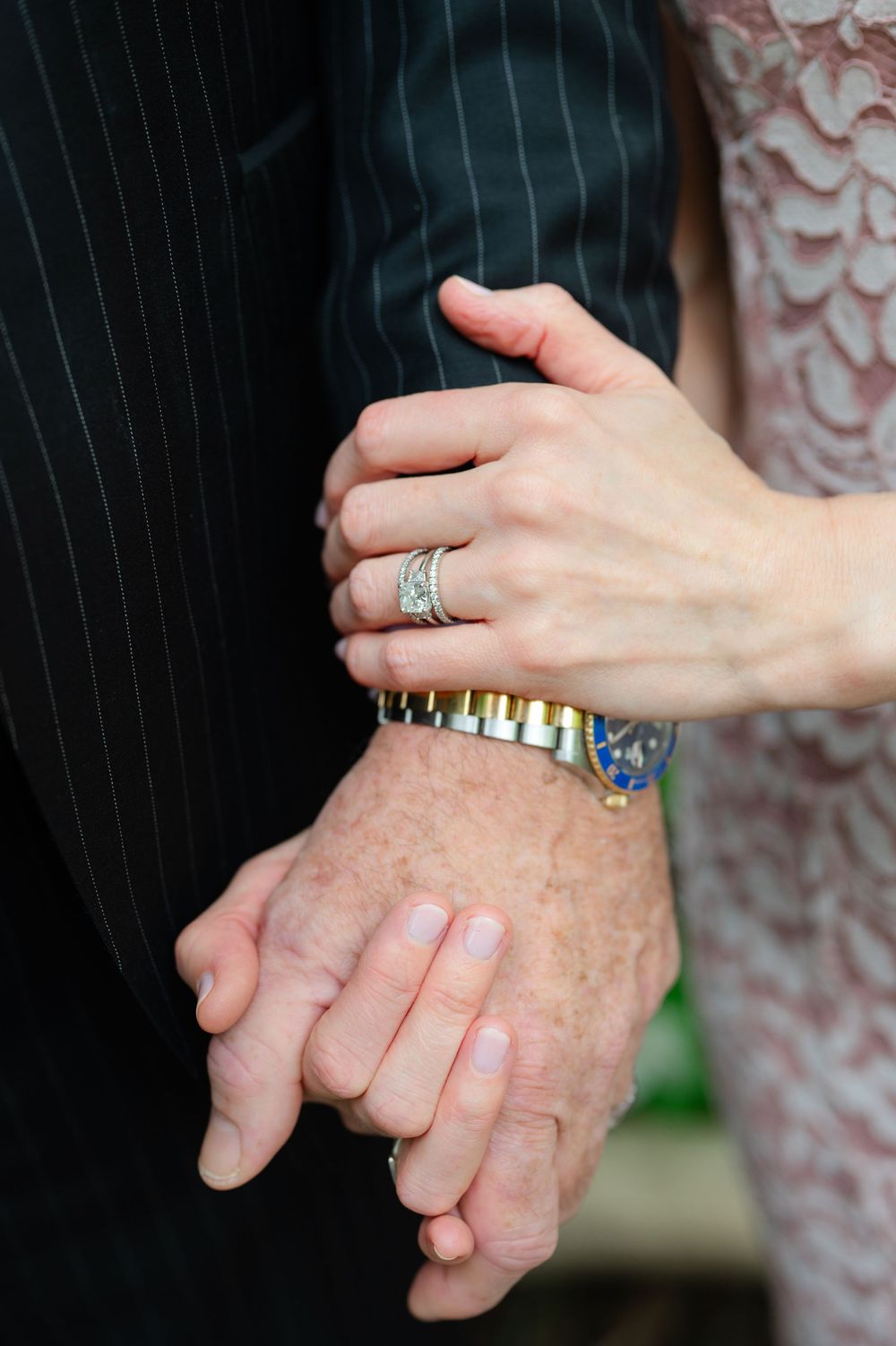 Close-up of couple holding hands showing diamond wedding rings and a gold Rolex watch at a wedding ceremony.