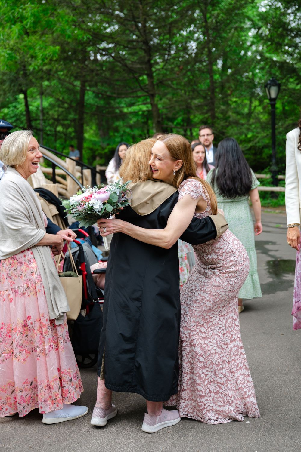 Wedding guests embracing and celebrating outdoors in Central Park with a bouquet of pink flowers.