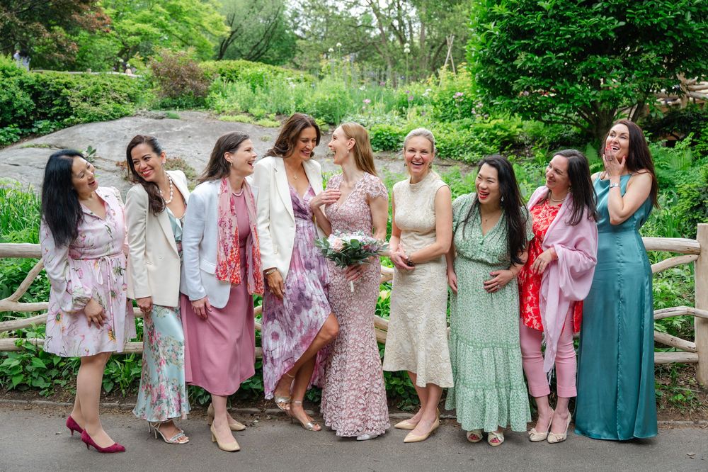 Bride in lace gown poses with bridesmaids in colorful dresses outdoors in Central Park, NYC.