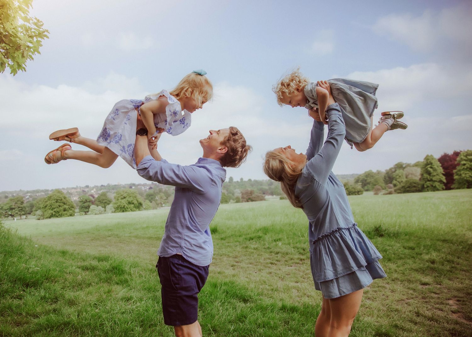 Family of four posing happily in a sunflower field, parents children wearing blue outfits. During a location family photoshoot in Bexley