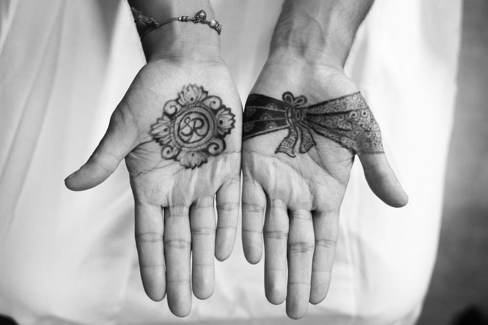 Black and white photo of two hands displaying palm tattoos, one with a mandala and one with a bow design.