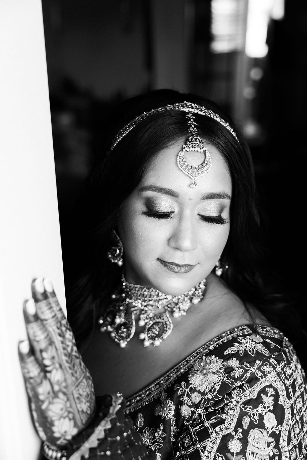 Black and white portrait of Indian bride wearing maang tikka and jeweled necklace with mehndi hands.