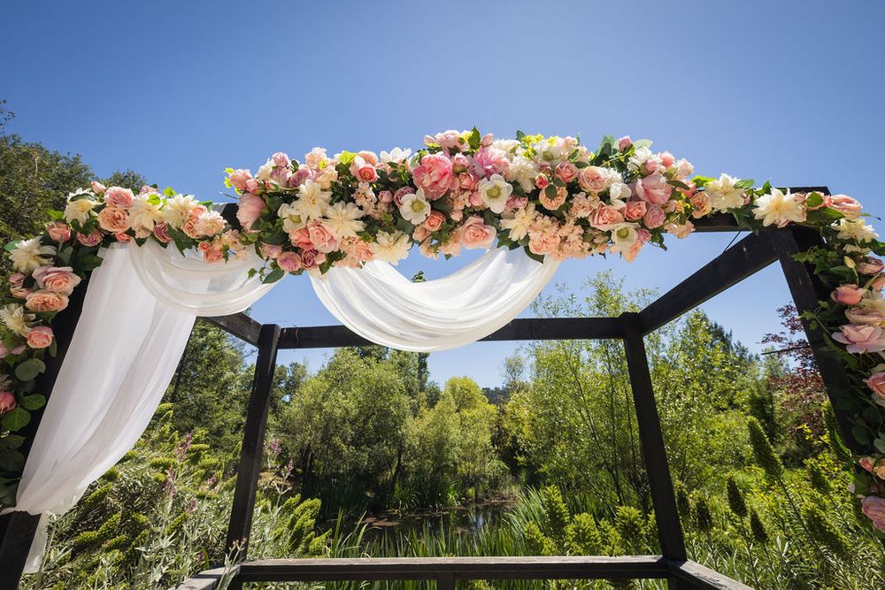 Floral wedding arch adorned with pink and white roses and draped white fabric against a blue sky.