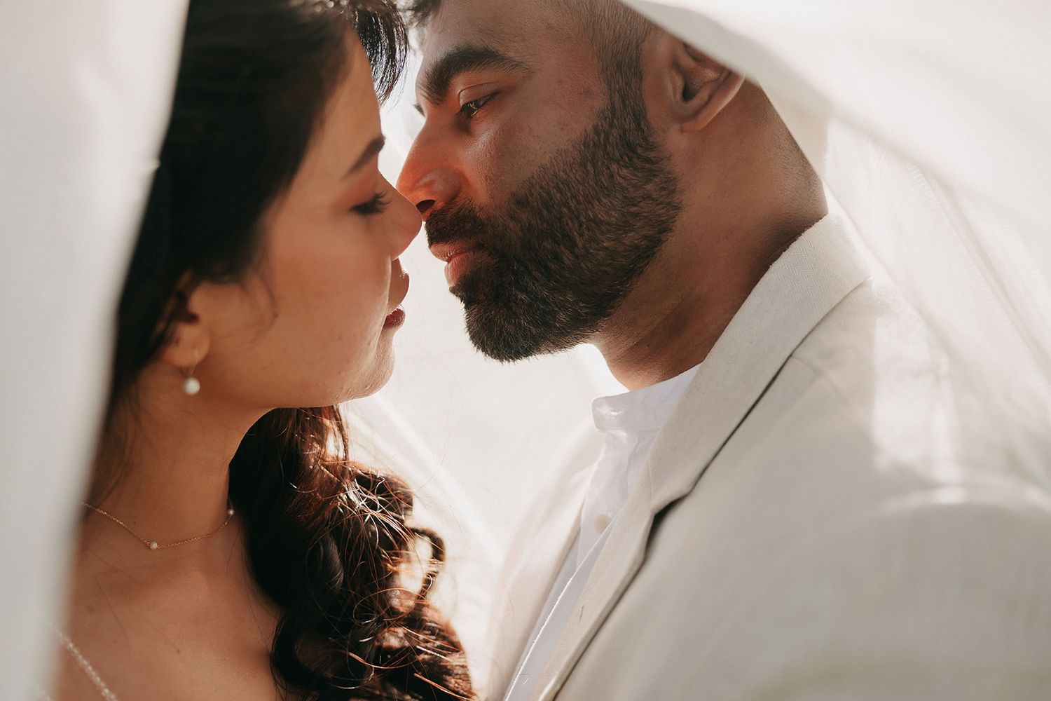 Intimate wedding couple moment captured against white background with soft lighting.