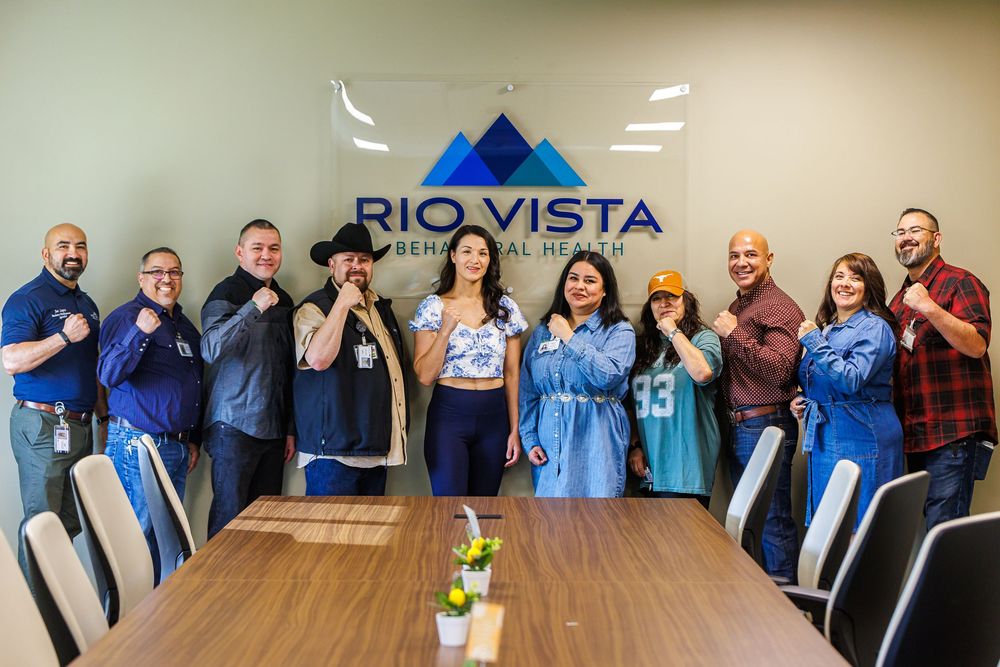 Group of smiling Rio Vista Behavioral Health staff posing together in a conference room, wearing sports jerseys and casual attire.