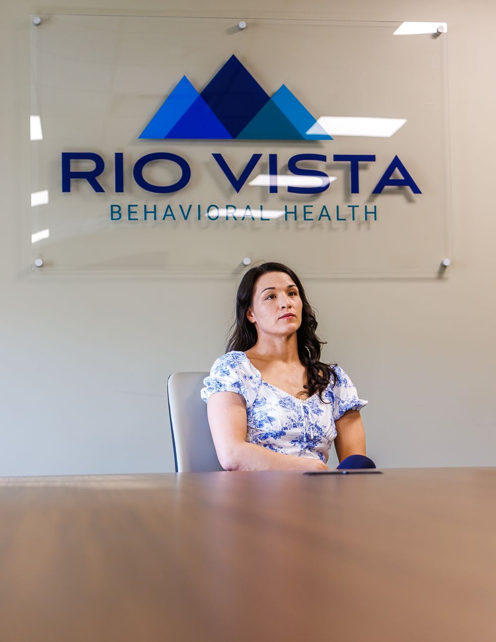 Woman sitting at a conference table inside Rio Vista Behavioral Health office, looking thoughtfully to the side.