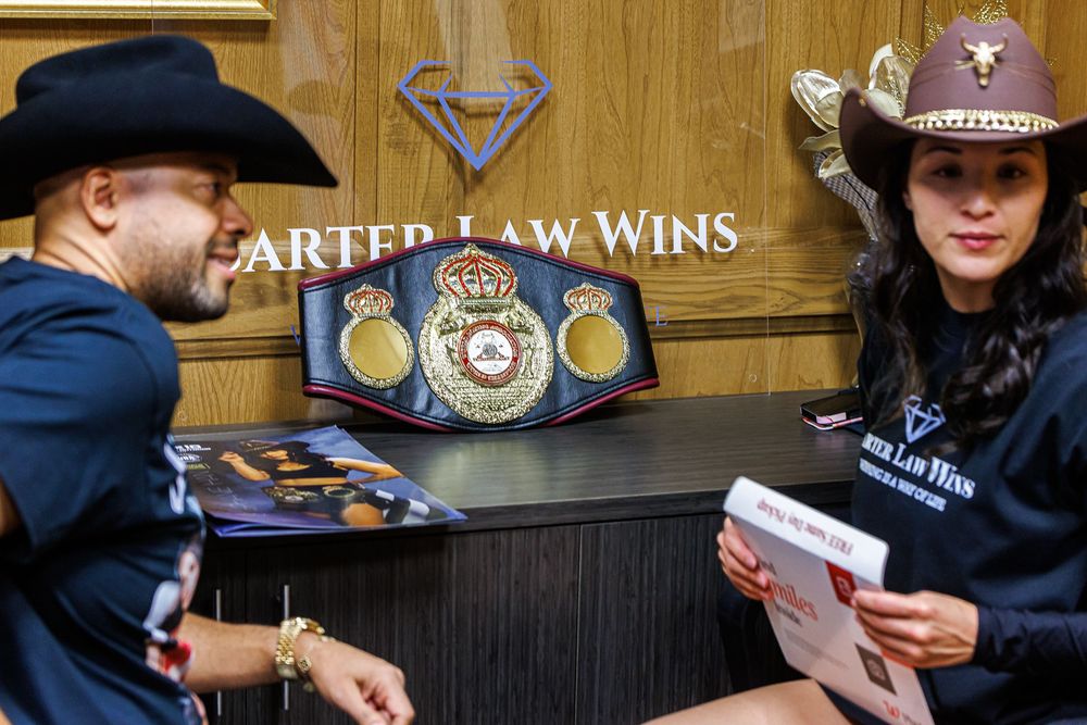 Two people in cowboy hats sit at a Carter Law Wins desk displaying a boxing championship belt.