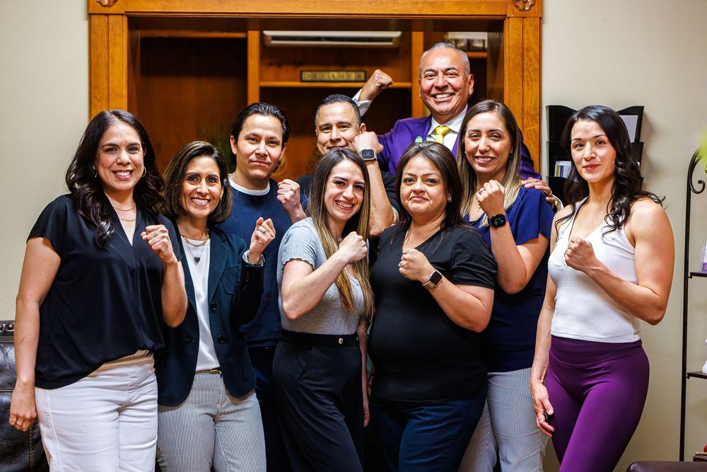Group of nine smiling professionals posing with fists raised in a modern office setting.