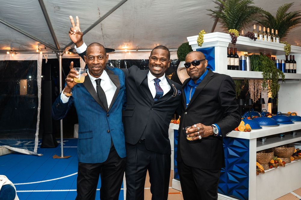 Three men in formal attire smile and pose together at an elegant blue and white themed event.