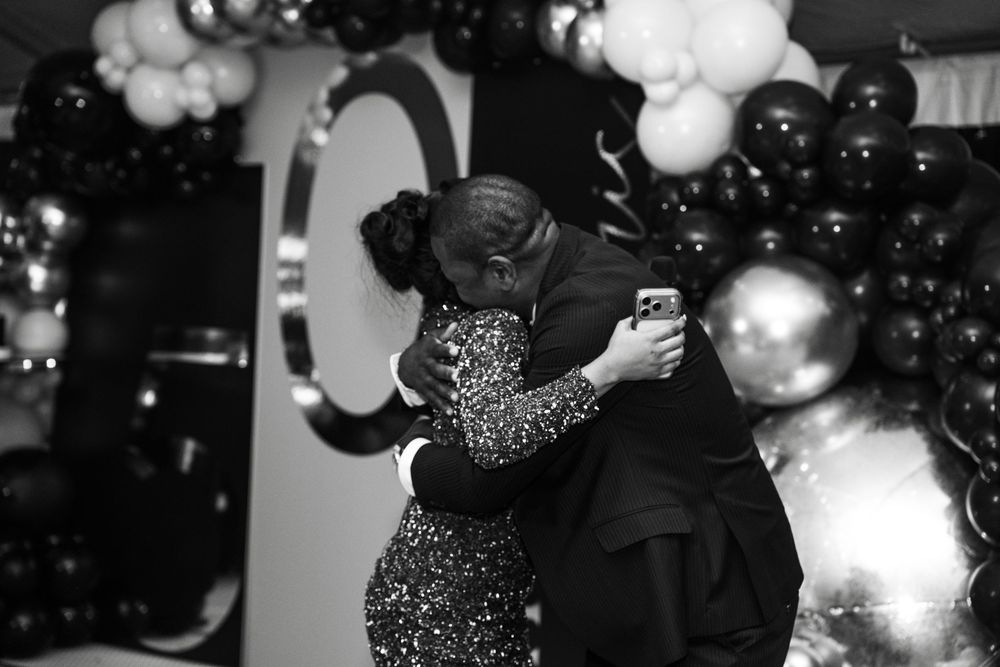 Couple embracing at elegant black and white balloon-decorated party celebration in formal attire.