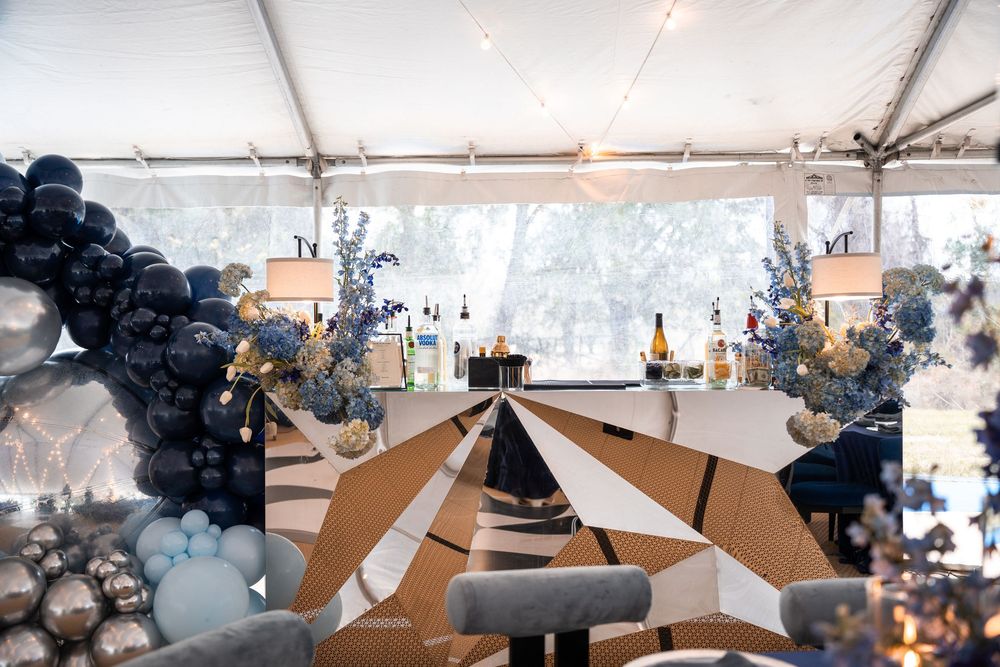 Luxurious event tent with navy balloon arch, geometric bar, floral arrangements, and champagne display.
