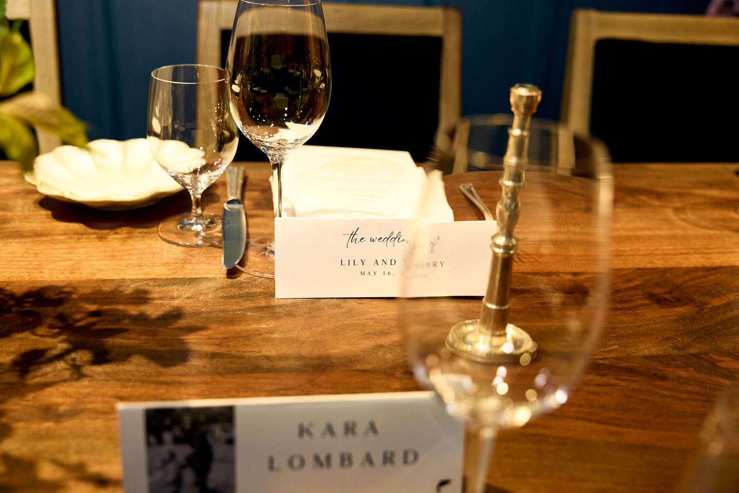 Elegant table setting with wine glasses, place cards for Kara Lombard and Lily Aid, on a rustic wooden table.