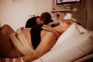 A partner comforts a laboring woman in a hospital bed while medical monitoring equipment is attached.