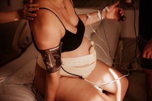 Pregnant woman in black sports bra with fetal monitors and blood pressure cuff during labor.