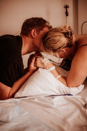 Supportive partner holding hands with laboring woman in hospital bed during childbirth.