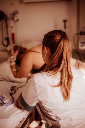 Midwife or nurse sitting bedside supporting woman through active labor in delivery room.
