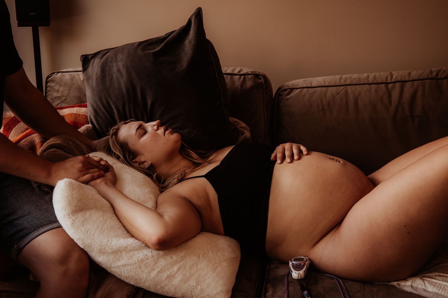 Pregnant woman resting on couch with partner providing comfort during labor.
