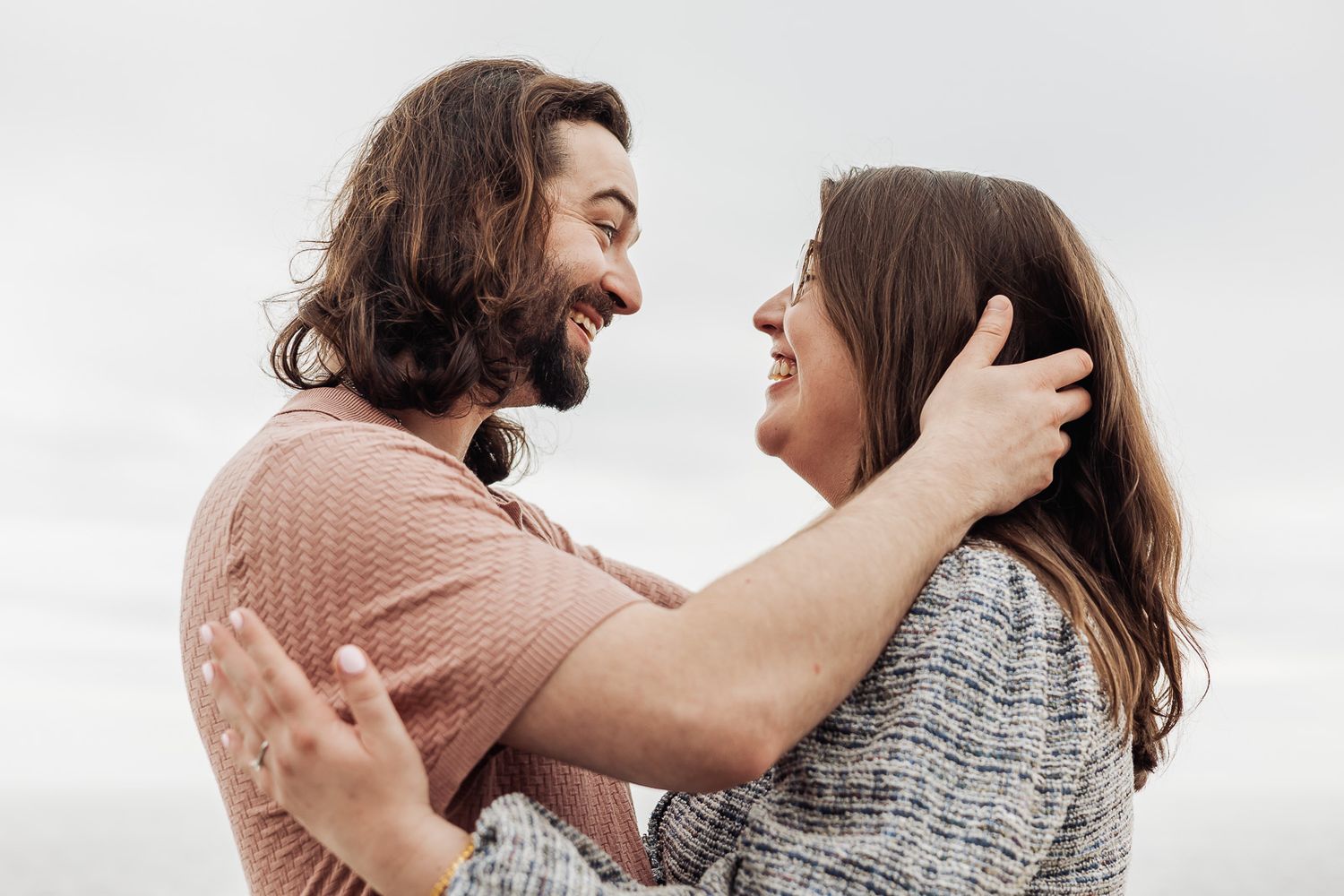 Happy couple embracing and smiling at each other outdoors against a cloudy sky background.