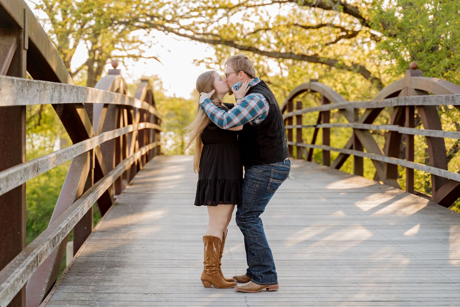Couple sharing a romantic kiss on a wooden bridge surrounded by autumn trees in golden hour light.