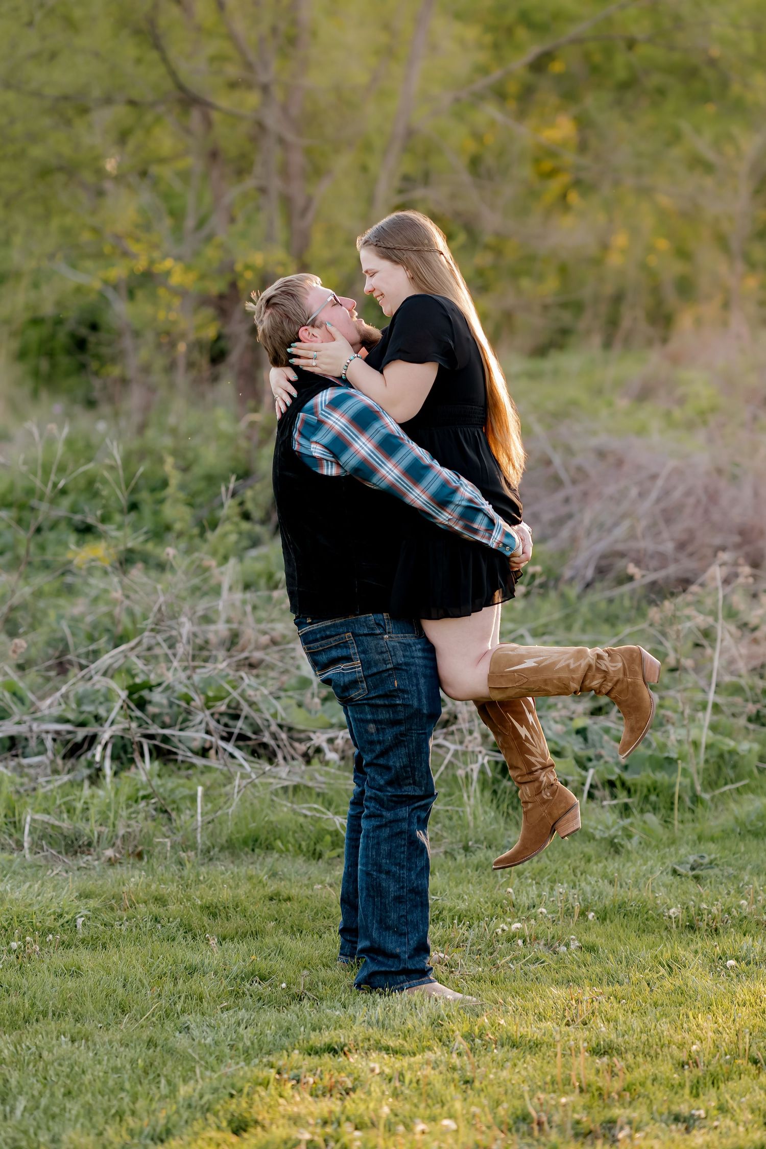 Man lifting woman in his arms for a kiss in a lush green field during a couples outdoor photo session.