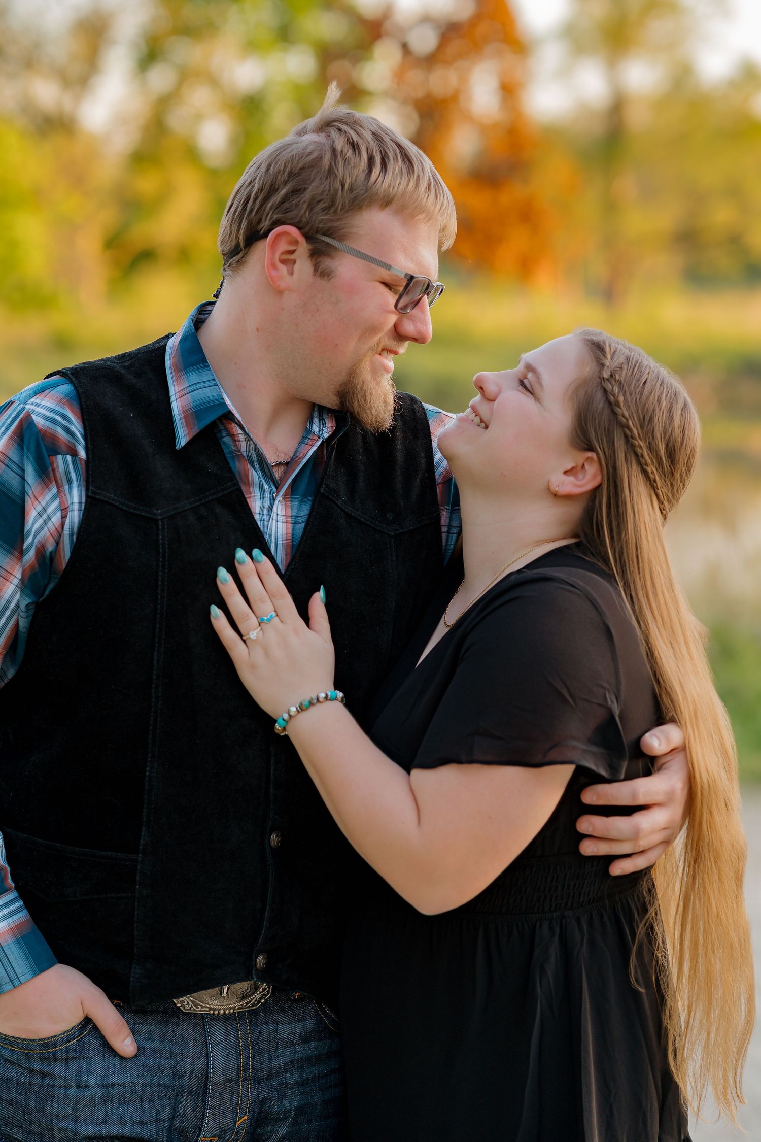 Couple gazing lovingly at each other outdoors, woman wearing engagement ring, in warm golden sunset light.
