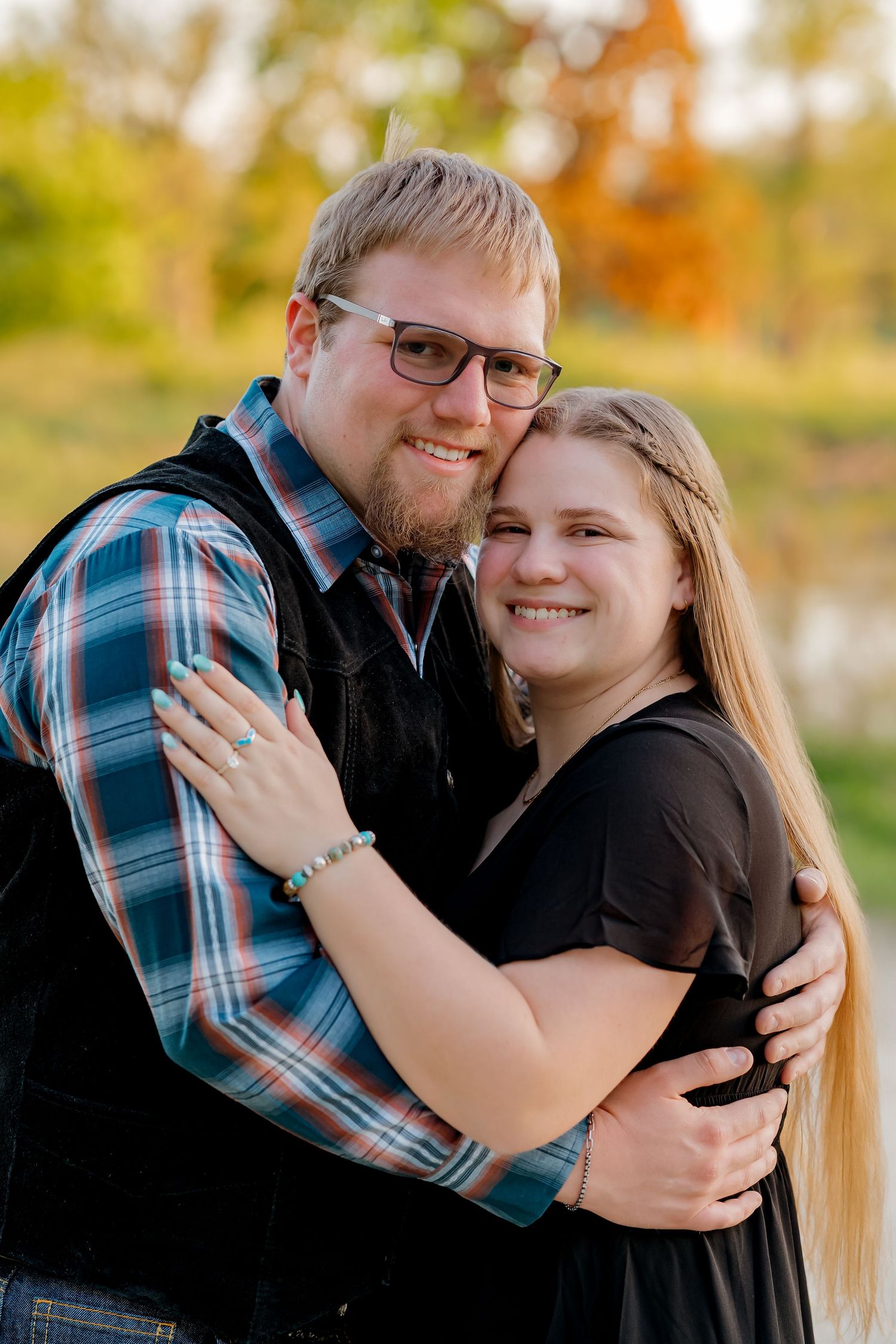 Happy couple embracing and smiling together in a warm outdoor engagement portrait at sunset.