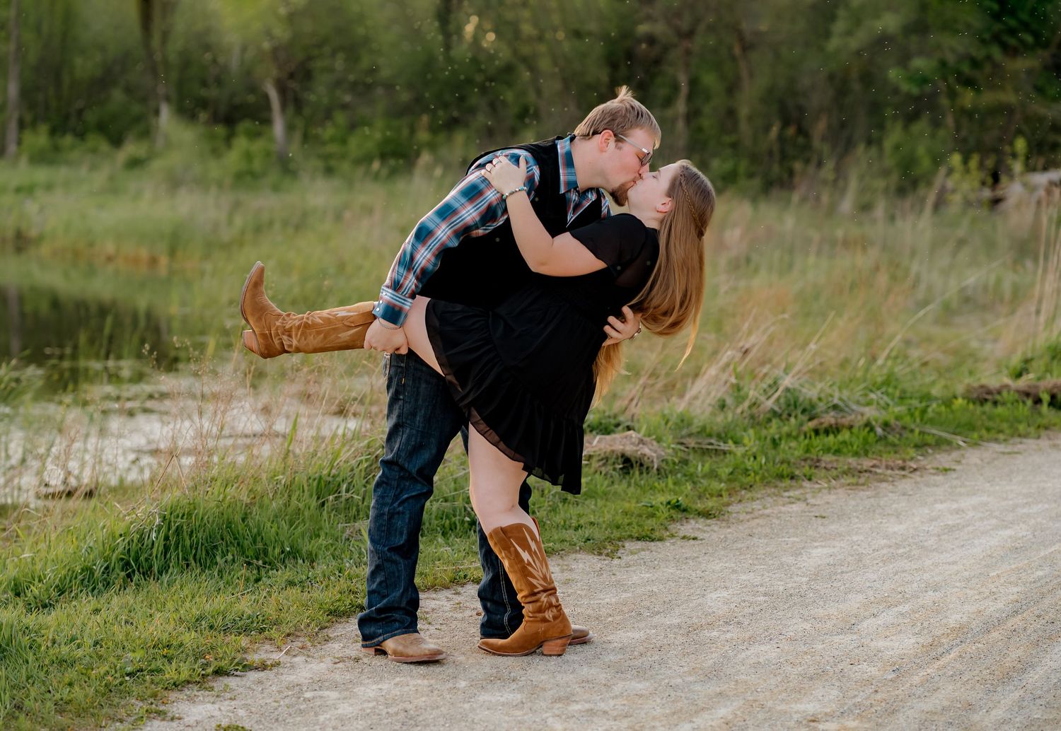 Couple sharing a romantic dip kiss on a scenic gravel path during outdoor engagement photos.