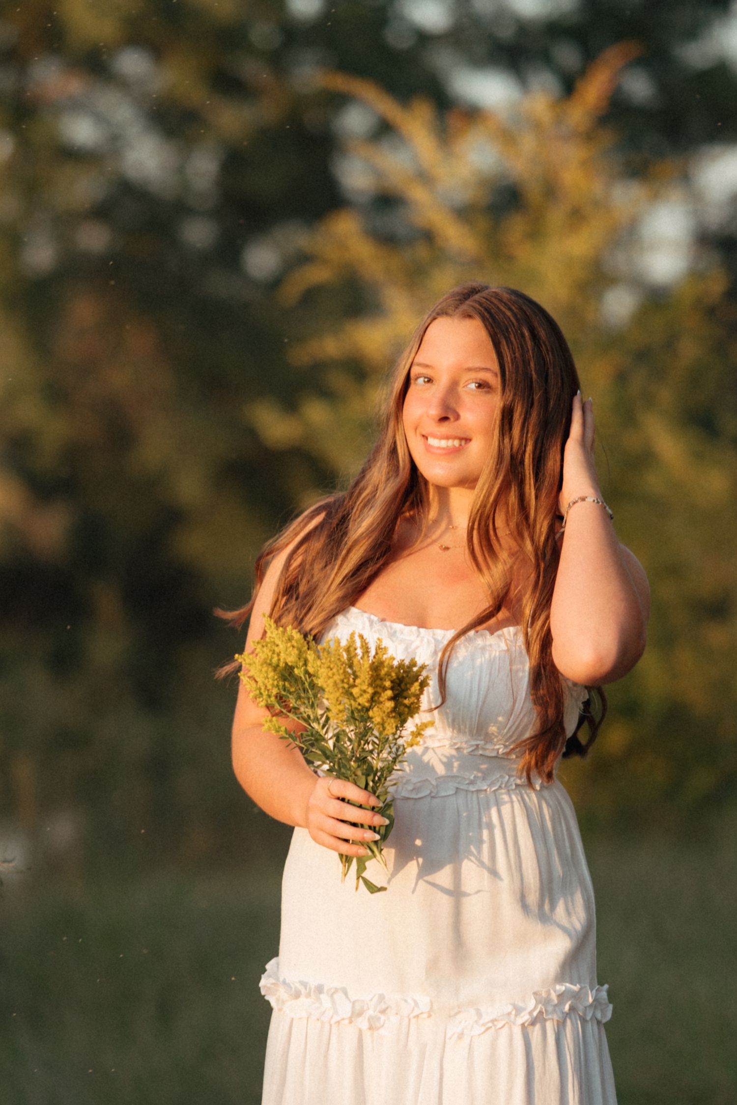 Senior girl in a white dress with flowers photographed outdoors with warm natural light and timeless Brookings SD senior portrait editing.