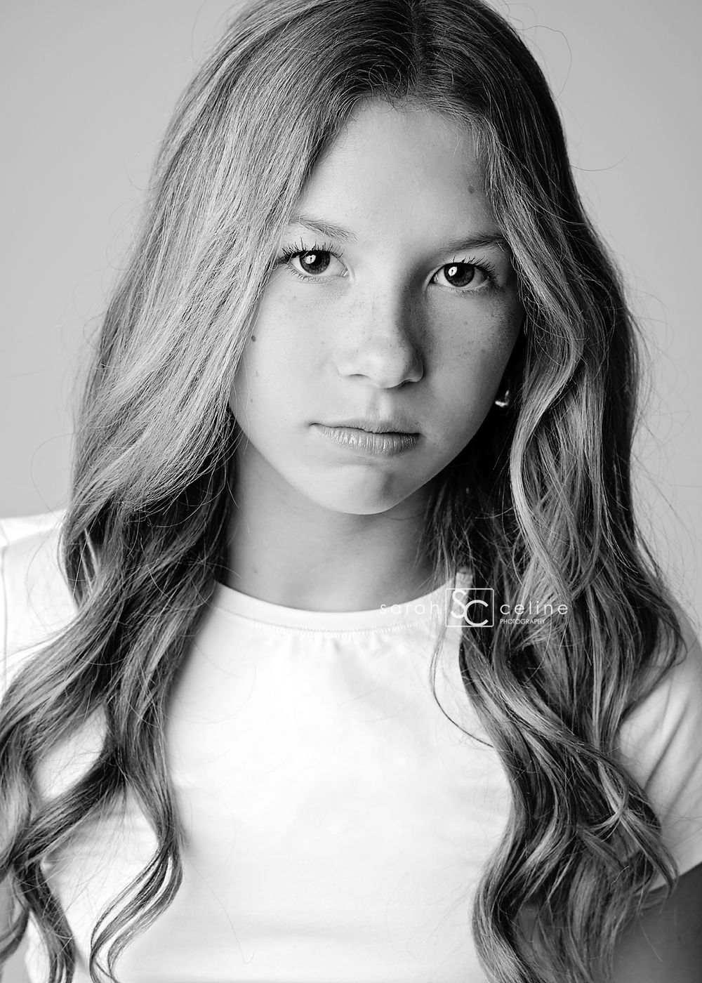 Black and white portrait of a young girl with long wavy hair wearing a white t-shirt.