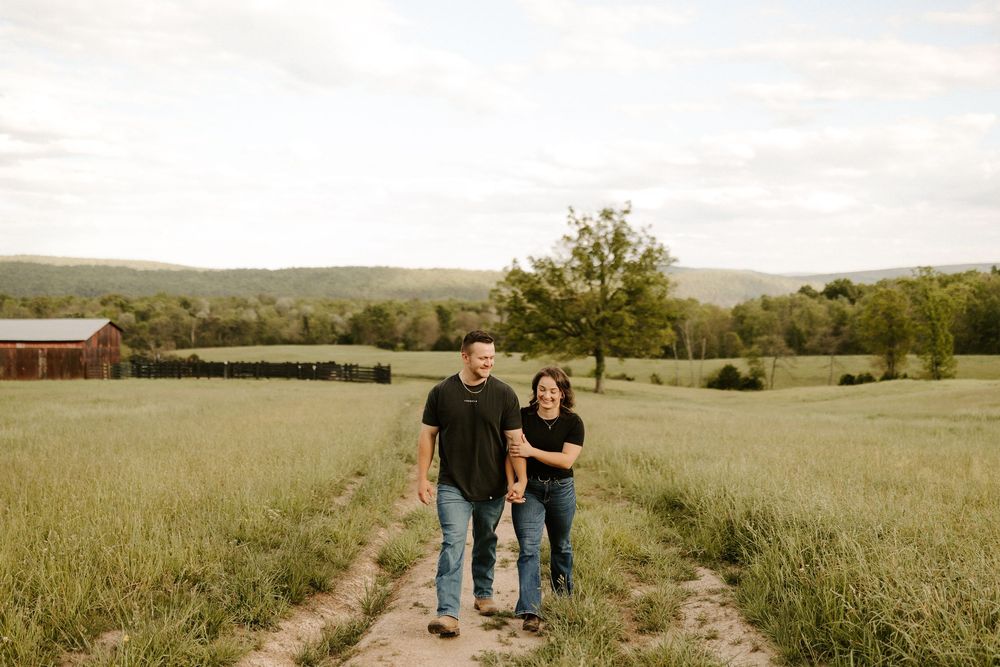 Happy couple walking hand in hand along a dirt path through a scenic green farm field.