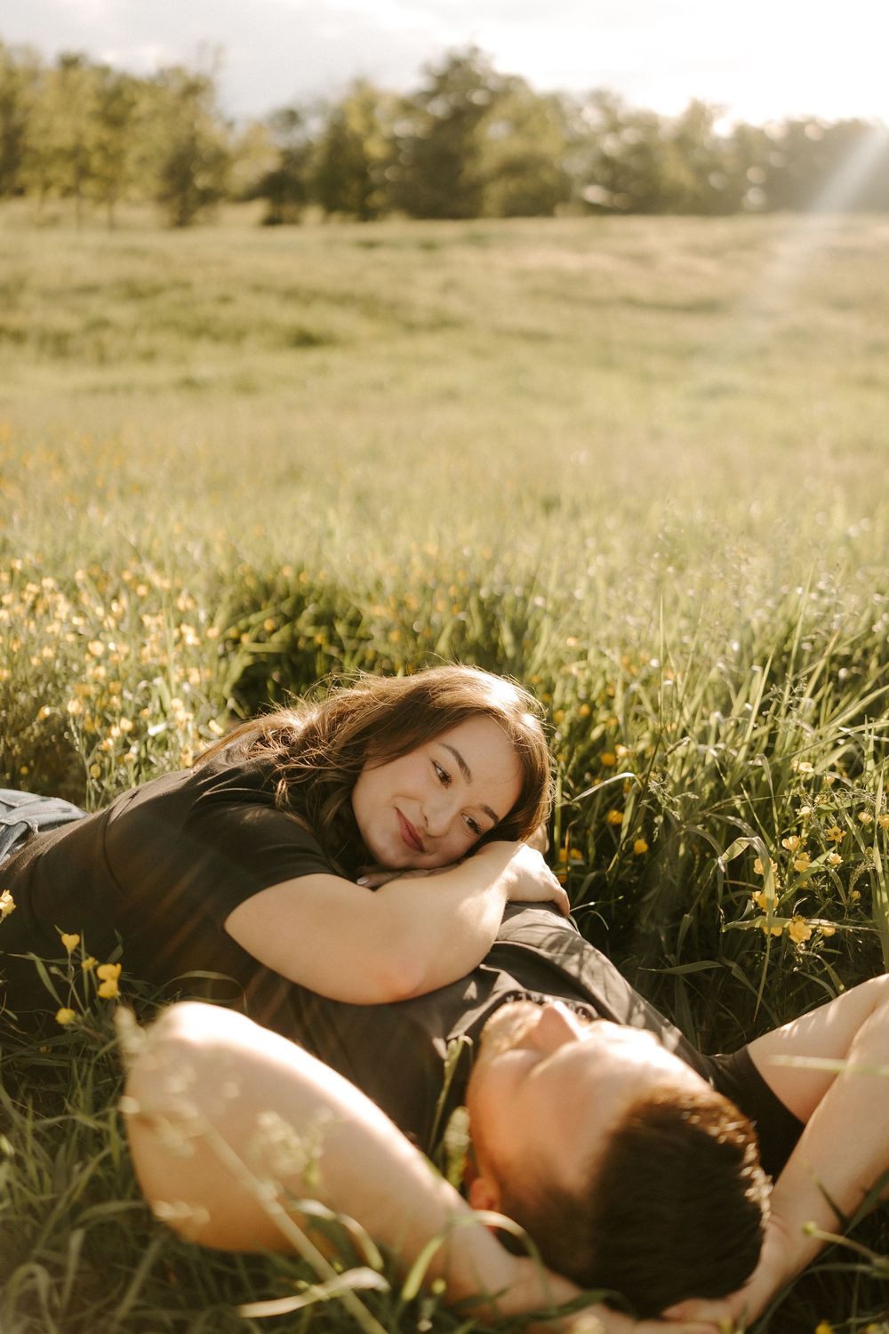 Woman resting her head on mans chest as they lay together in a wildflower field.