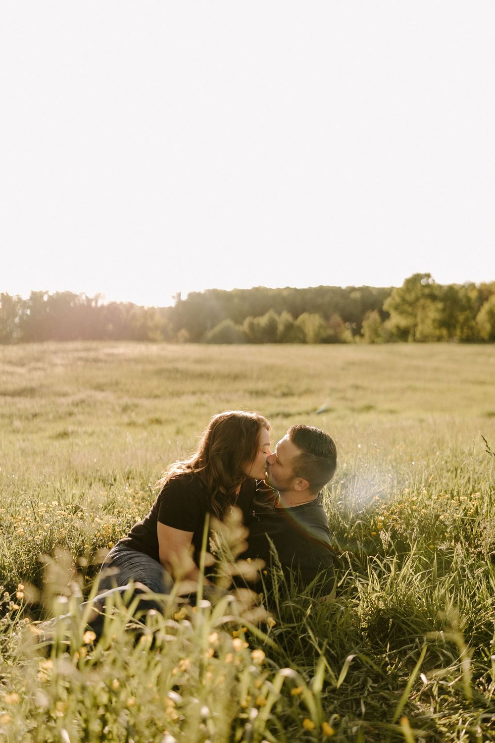 Couple kissing while lying in a sun-drenched meadow with wildflowers in the foreground.