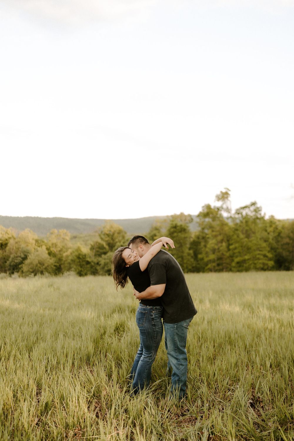 Couple sharing a kiss while embracing in a lush green field during golden hour engagement session.