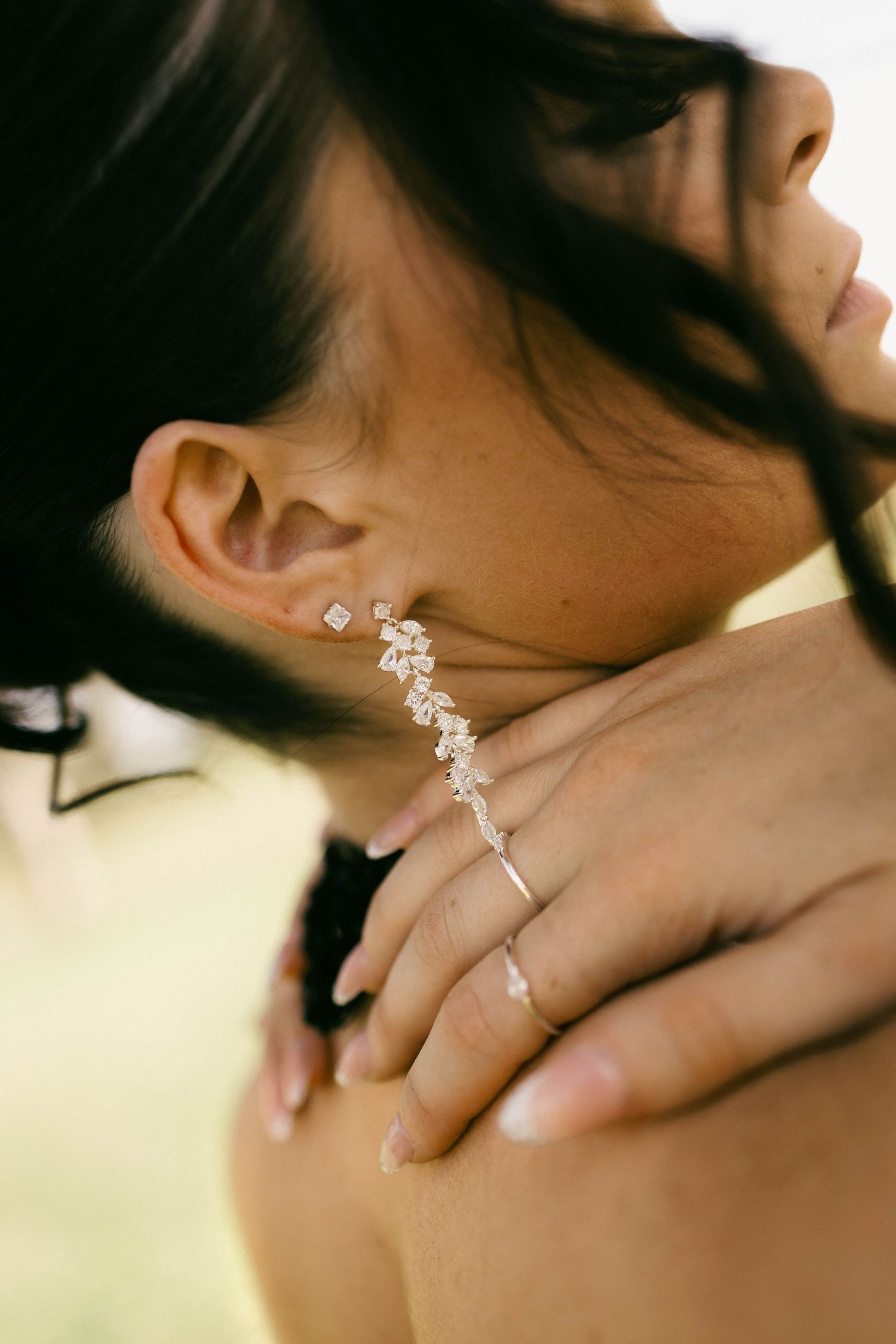 Close-up of a woman wearing an elegant crystal drop earring and delicate ring with French manicure.