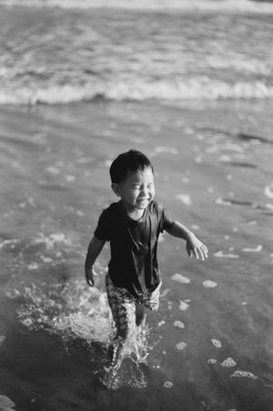 Joyful young boy splashing in ocean waves at the beach in black and white photo.