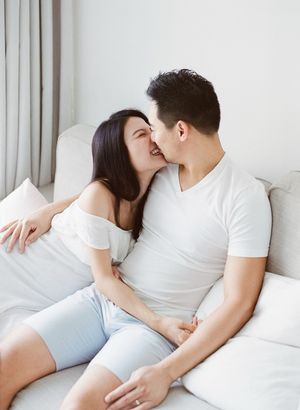 A couple sharing a tender kiss while sitting together on a white sofa in a bright room.