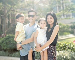 Happy Asian family of four smiling together outdoors in warm sunlight.