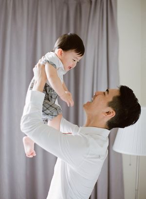 Father joyfully lifting smiling baby up in the air in bright room.