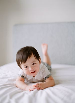 Adorable baby lying on white bed smiling at camera with legs raised.