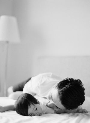 Tender black and white photo of father lying on bed with infant child.