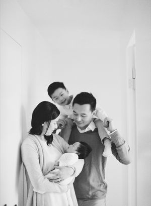 Black and white family portrait with parents holding newborn and young child.